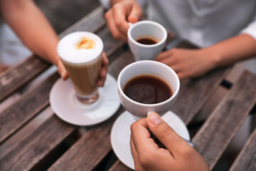 Friends drinking coffee at wooden table in outdoor cafe, closeup