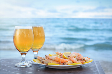Cold beer in glasses and shrimps served with lemon on beach
