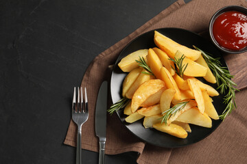 Plate with tasty baked potato wedges, rosemary and sauce on black table, top view. Space for text