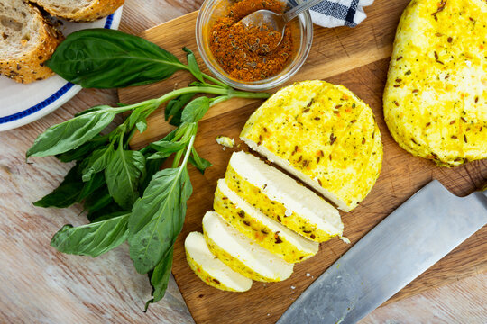 Slices of spicy roasted cottage cheese seasoned with turmeric and cumin seeds on wooden cutting board served with whole-grain baguette and greens. Healthy breakfast concept