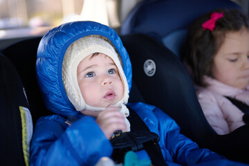 siblings in winter coats sitting in safety chairs in the car