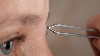 woman plucking eyebrows with tweezers closeup - obrazy, fototapety, plakaty