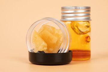 glass jar with brown cannabis wax, pieces of hardened resin of marijuana extract on an orange...