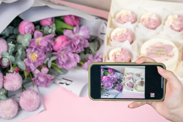 Photo on phone of freshly cupcakes and beautiful flowers on a table.