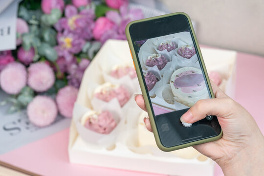 Photo on phone of freshly cupcakes and beautiful flowers on a table.
