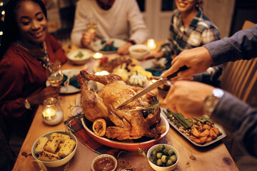 Close up of man carving turkey meat while having dinner with friends on Thanksgiving. - obrazy, fototapety, plakaty
