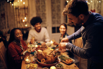 Smiling man carving Thanksgiving turkey during dinner in dining room.