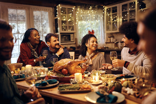 Multiracial group of friends have fun while talking during Thanksgiving dinner at dining table.