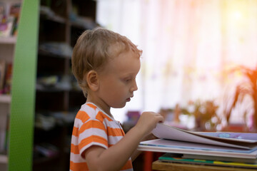 A preschooler examines a book in the reading room, a boy reads a children's book. Library