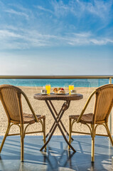 Table with breakfast and two chairs on a hotel balcony by the beach - Travel concept