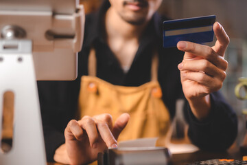 Closeup of young Asian barista wearing an orange apron uniform filling bank debit and credit card...