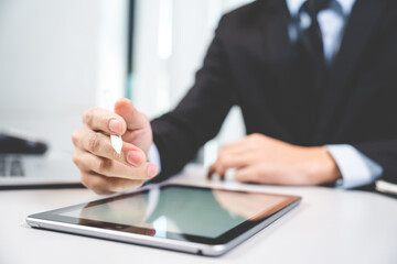 Closeup of hands of a successful business man and entrepreneur in formal clothing sitting in modern lighted office while holding pen and using digital tablet and reading document and making edits