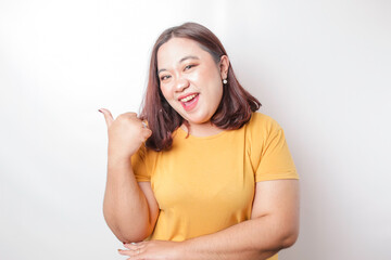 Excited Asian big sized woman wearing yellow shirt gives thumbs up hand gesture of approval, isolated by white background