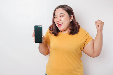 A portrait of a happy Asian big sized woman is smiling and showing copy space on her smartphone wearing yellow shirt isolated by a white background