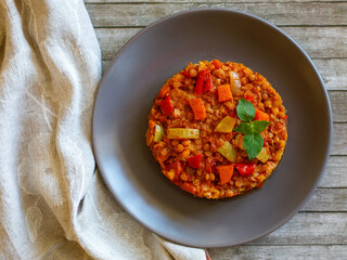 Healthy vegetarian homemade lentil stew with vegetables on a plate with basil leaf on rustic wooden table with napkin. Vegan diet. Top view, flat lay