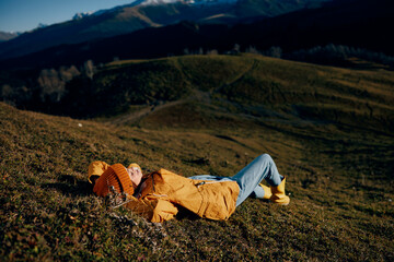 Woman beautifully lying on a hill recreation smile with teeth in the mountains in the autumn in a yellow raincoat and jeans happy sunset trip to hike the mountains in the snow, freedom lifestyle 
