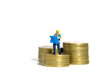 Miniature people toy figure photography. Project budget concept. A construction worker with blueprint building standing above golden coin money pile. Isolated on white background - Powered by Adobe