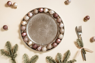 Christmas table setting concept, shining small Christmas balls beige pink color in metal plate, knife, fork decorated green branches fir tree, New Year holiday dinner or party idea