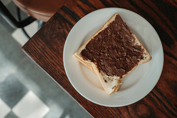 Flat lay or top view shot of a bread with chocolate sauce as breakfast in a white plate and wooden table