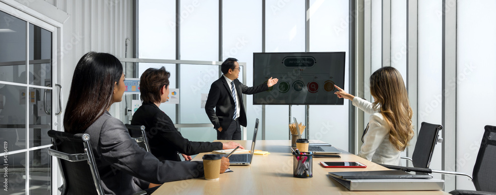 Wall mural asian senior manager in black suit giving presentation with large digital monitor. business executiv