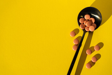 Pharmaceutical tablets in a spoon on a yellow background. Tablets or vitamins to maintain immunity on a yellow background. The concept of healthcare, nutritional supplements for a healthy and fulfilli