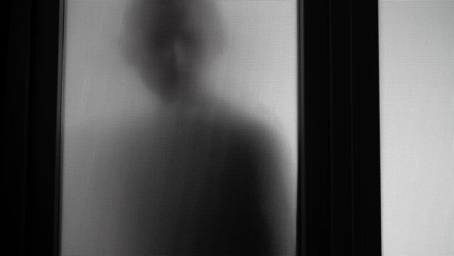 The man approaches the glass opaque door and leaves. An uninvited guest at the door. Shadow of an intruder