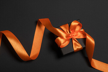 Black gift box with orange ribbon on a black background