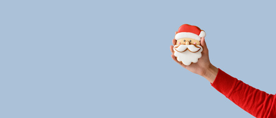 Female hand holding tasty Christmas cookie on light blue background with space for text