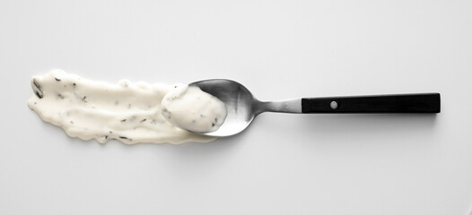 Spoon with spilled Caesar sauce on light background