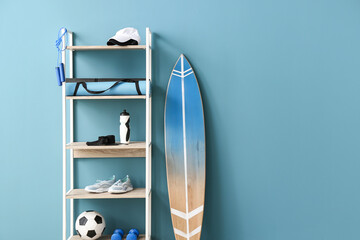 Shelf unit with sport equipment and surfboard near color wall