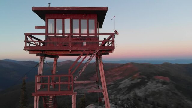 Aerial footage of a girl standing on a lookout tower in North Idaho