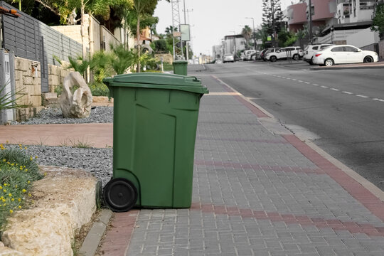 Green garbage container near road in city