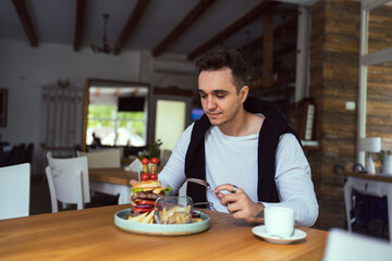 Fototapeta na wymiar one young man sit at table eat burger and chips at restaurant