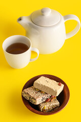 Bowl with tasty sesame halva, cup of tea and teapot on yellow background