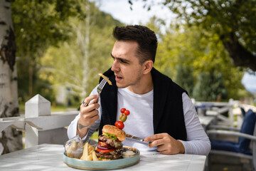one young man sit at table eat burger and chips at restaurant outdoor