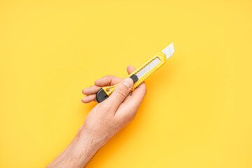 Man with utility knife on yellow background