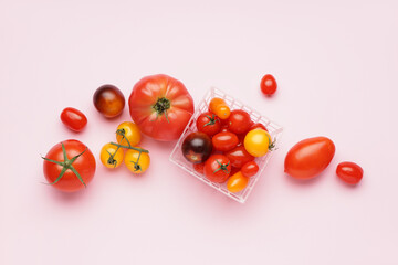 Basket with different fresh tomatoes on pink background