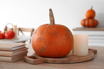 Board with pumpkin, burning candles and books on counter in kitchen