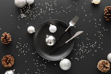 Beautiful table setting with Christmas balls and fir cones on black background