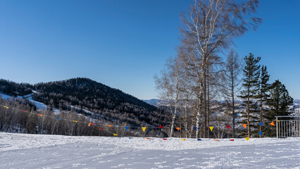 Fototapeta premium A high-altitude plateau in a ski resort. Multi colored flags are stretched along the edge. Mountains against a clear blue sky. Altai. Manzherok