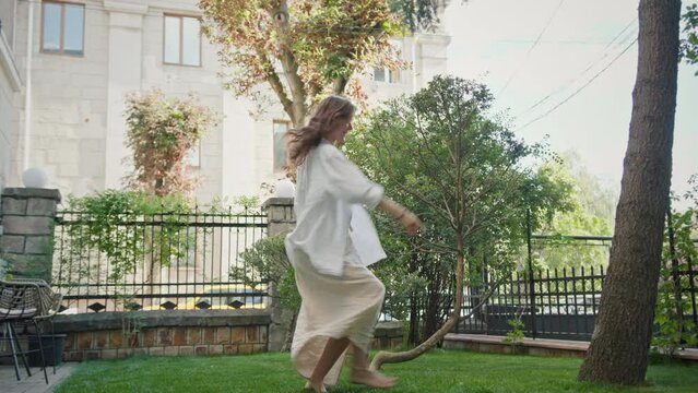 Young slim woman dances barefoot on green lawn of office building