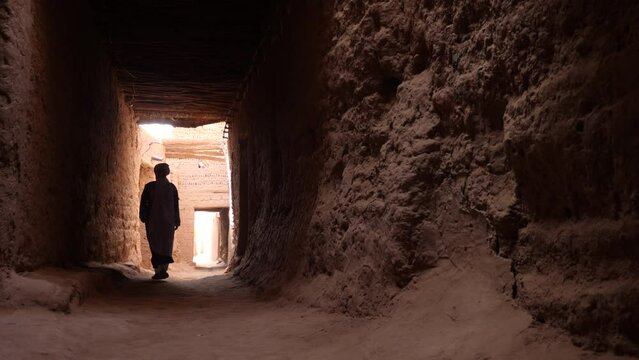 A traditional dressed Bedouin Moroccan man wearing a blue gandoura and a turban walks inside the Kasbah in Mhamid, Morocco. Authentic rural scene of South Morocco. 4k.