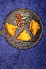 Samosa or Singara with chutney on black plate. top view