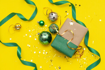 Composition with Christmas gift, balls and ribbon on yellow background