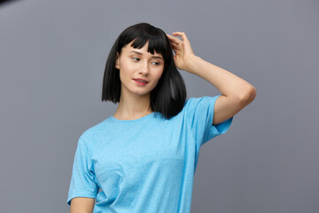 a calm woman stands against a dark background in a blue T-shirt looking down, adjusting her hair with her fingertips