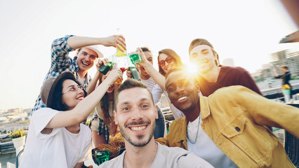 Obraz premium Point of view shot of handsome guy holding camera and taking selfie while his friends having fun