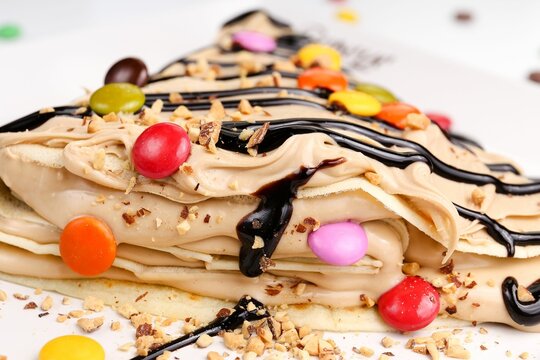 Close-up view of rFench crepes with colorful candies and chocolate syrup topping