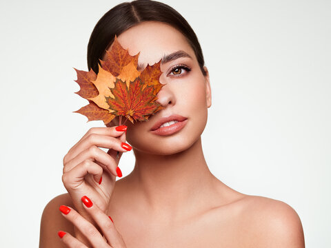 Portrait of beautiful young woman with autumn maple leafs. Healthy clean fresh skin natural make up beauty eyes and red nails