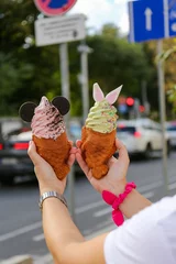 Fotobehang Vertical view of hands holding green and pink Taiyaki ice creams with cute dressings © Nina Ljusic/Wirestock Creators