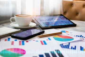 Latte coffee in white cup and tablet computer with chart on screen and mobile phone, paperwork, business people analysis of investment plan and money exchange, Double explosure of digital chart